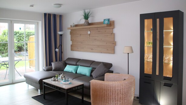 A modern living room with a grey sofa, a coffee table, a wicker chair, and a black cabinet with glass doors. - Fantastic FH, on the dike, incl. Indoor pool use, play barn + lagoon free  (Butjadingen)