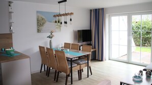 A modern dining area with a table, chairs, and a television. - Fantastic FH, on the dike, incl. Indoor pool use, play barn + lagoon free  (Butjadingen)