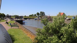 A riverside view with boats, a pedestrian path, and greenery. - Fantastic FH, on the dike, incl. Indoor pool use, play barn + lagoon free  (Butjadingen)