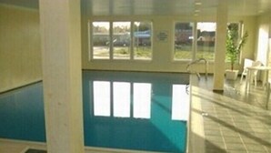 A swimming pool with a view of the outside, a white chair, and a tiled floor. - Fantastic FH, on the dike, incl. Indoor pool use, play barn + lagoon free  (Butjadingen)