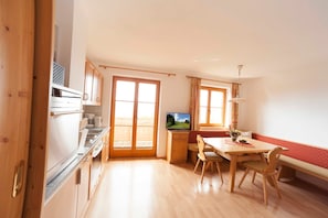 Una cocina con estufa, horno y microondas, un comedor con mesa y sillas, y un televisor sobre un mueble.