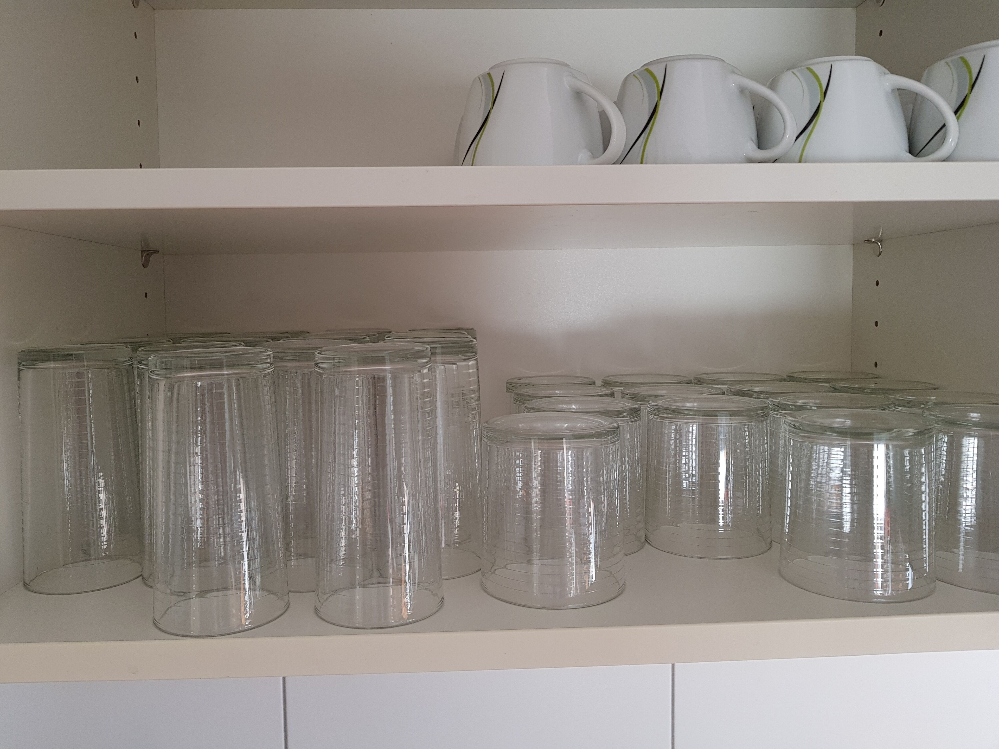 Une étagère de cuisine avec des bocaux en verre transparent et des tasses en céramique blanche.