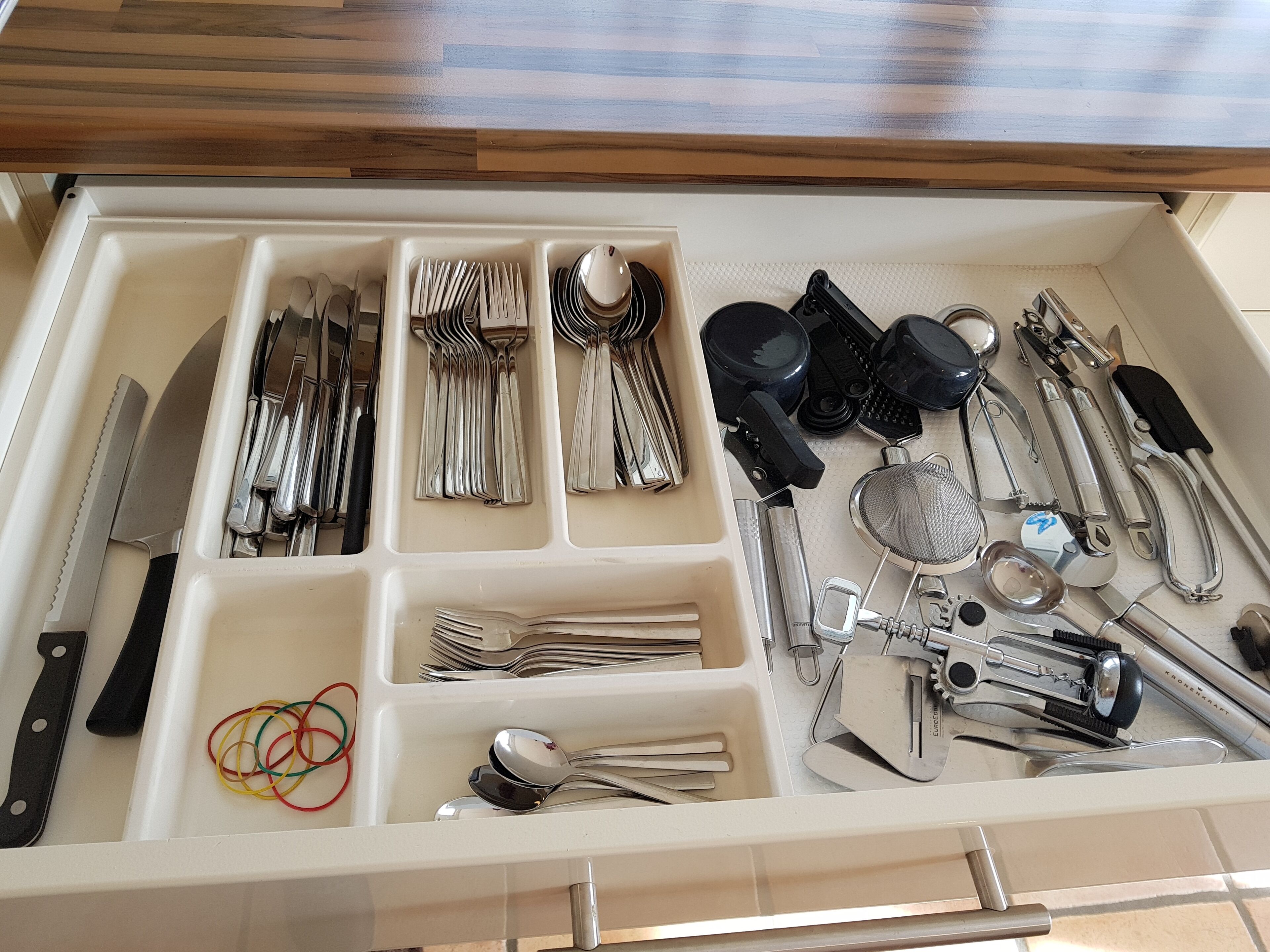 A drawer with compartments containing various kitchen utensils, including knives, forks, spoons, and a grater.