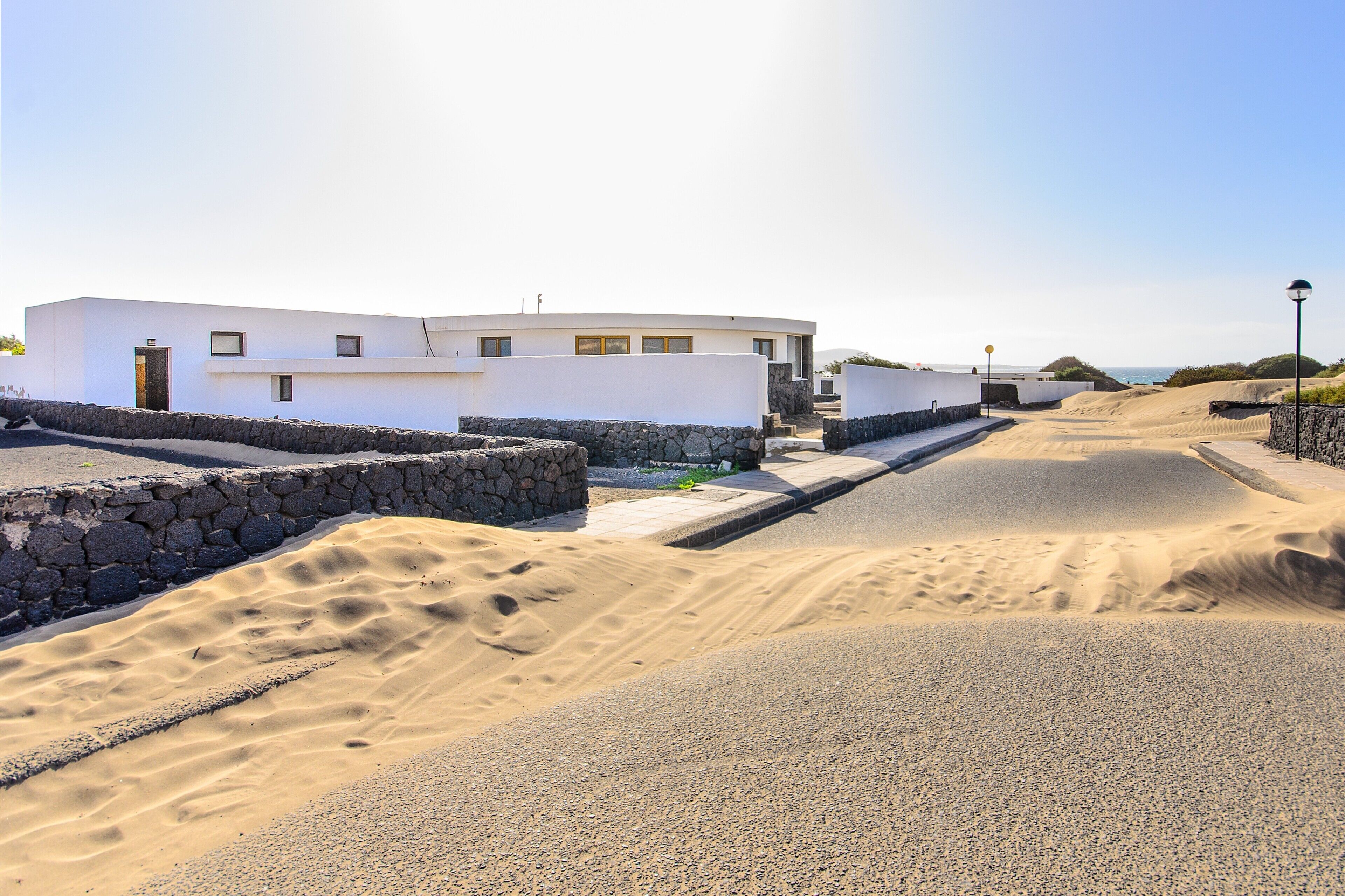 A modern building with a flat roof, a stone wall, and a paved road.