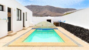 Une piscine dotée d’une structure en verre, de murs blancs et offrant une vue sur une montagne.