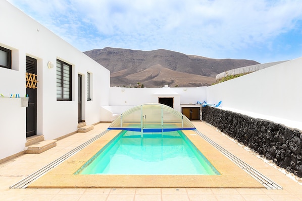 Una piscina con cerramiento de vidrio, paredes blancas y vistas a la montaña.
