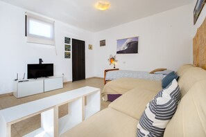 Un dormitorio con una cama, un televisor sobre un mueble blanco, una ventana y una obra de arte colgada en la pared.