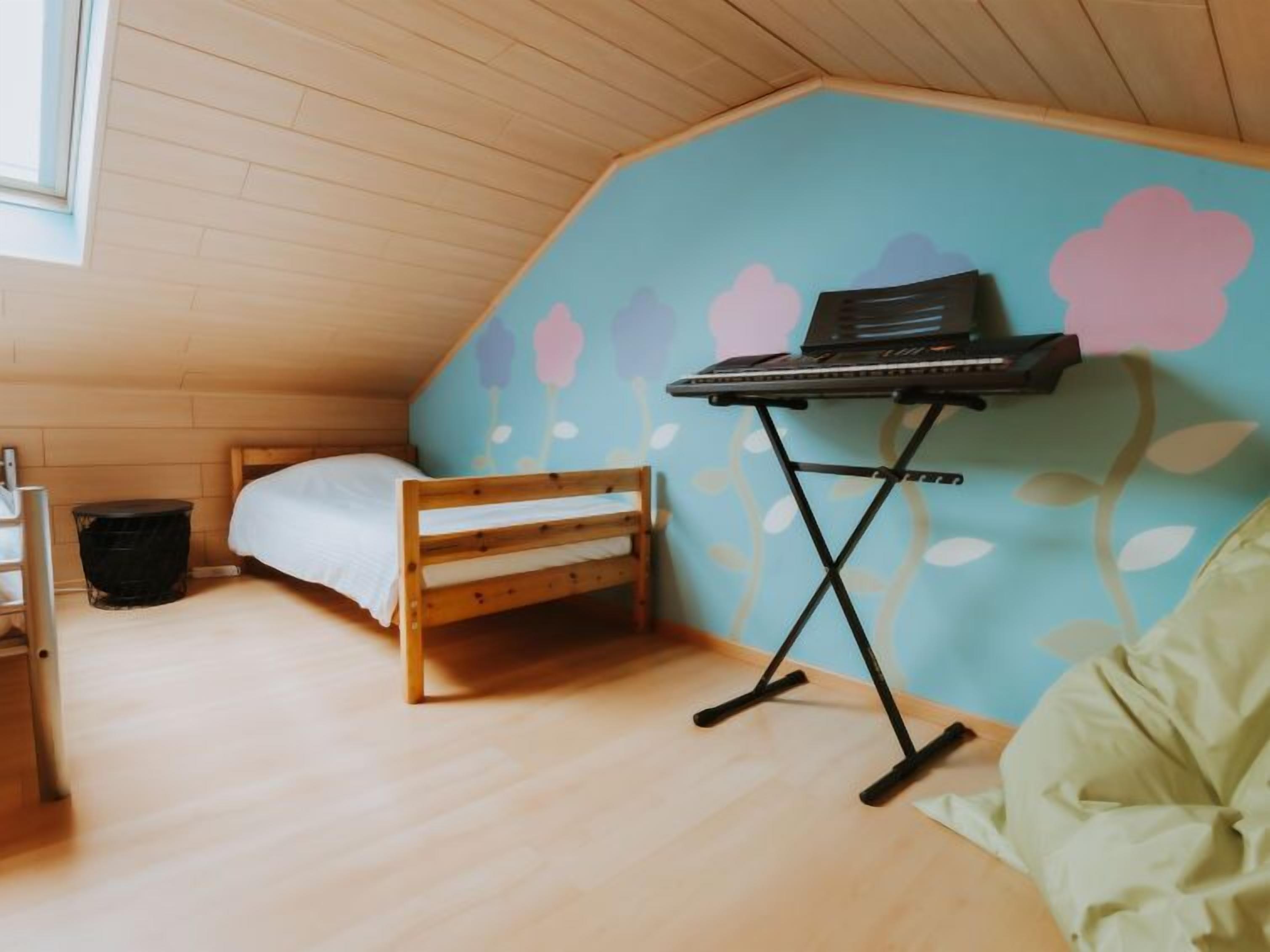 Una camera da letto soffitta accogliente e intima, con soffitto spiovente, un letto singolo, una piccola panca in legno e un portatile su un supporto.