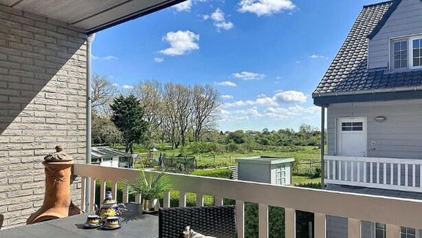 En balkong med ett bord och stolar, utsikt över ett hus och en klar himmel.