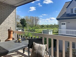 A balcony with a table and chairs, a view of a house, and a clear sky.