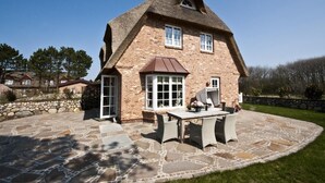 Ein Haus mit einzigartigem Strohdach und Backsteinfassade, mit einer Terrasse, die mit Steinplatten und Gartenmöbeln ausgestattet ist.