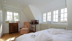 Ein Schlafzimmer mit einem großen Bett, einem Schminktisch, einem Sessel und einem Fernseher.