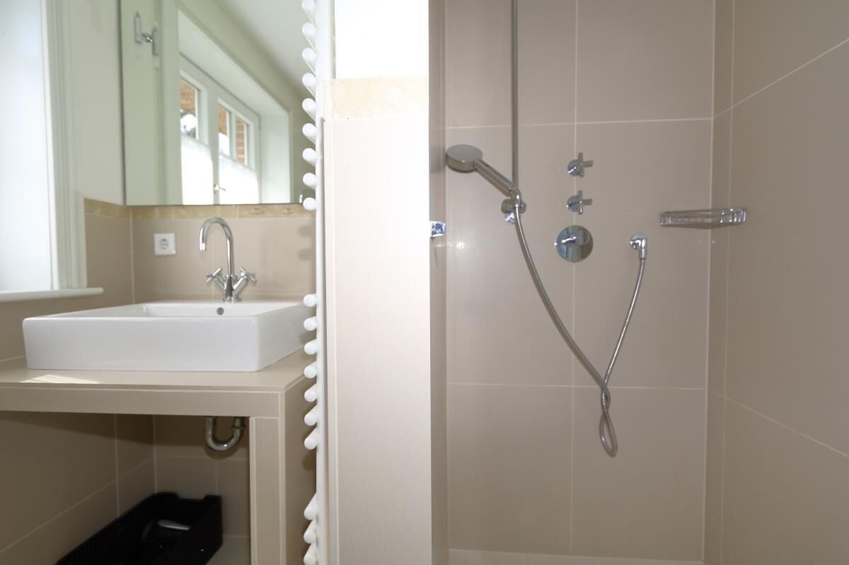 Un baño con un lavamanos blanco, un espejo y una ducha con cabezal de ducha de mano y grifo empotrado.
