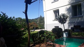 Un patio trasero con piscina, una jardinera de barril de madera y un jardín con diversas plantas.