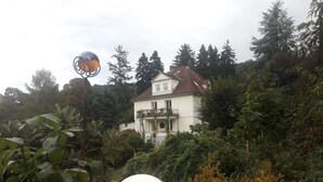 Una casa de dos pisos rodeada de abundante vegetación y árboles.