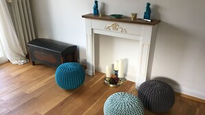 Una habitación con chimenea, suelo de madera y tres otomanas tejidas en diferentes colores.