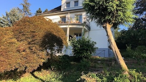 Una casa de dos pisos con un balcón, rodeada de árboles y vegetación.