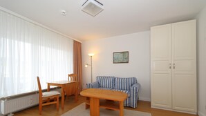 Una habitación con una mesa y sillas de madera, un sofá a rayas, un radiador, un armario blanco y un cuadro en la pared.