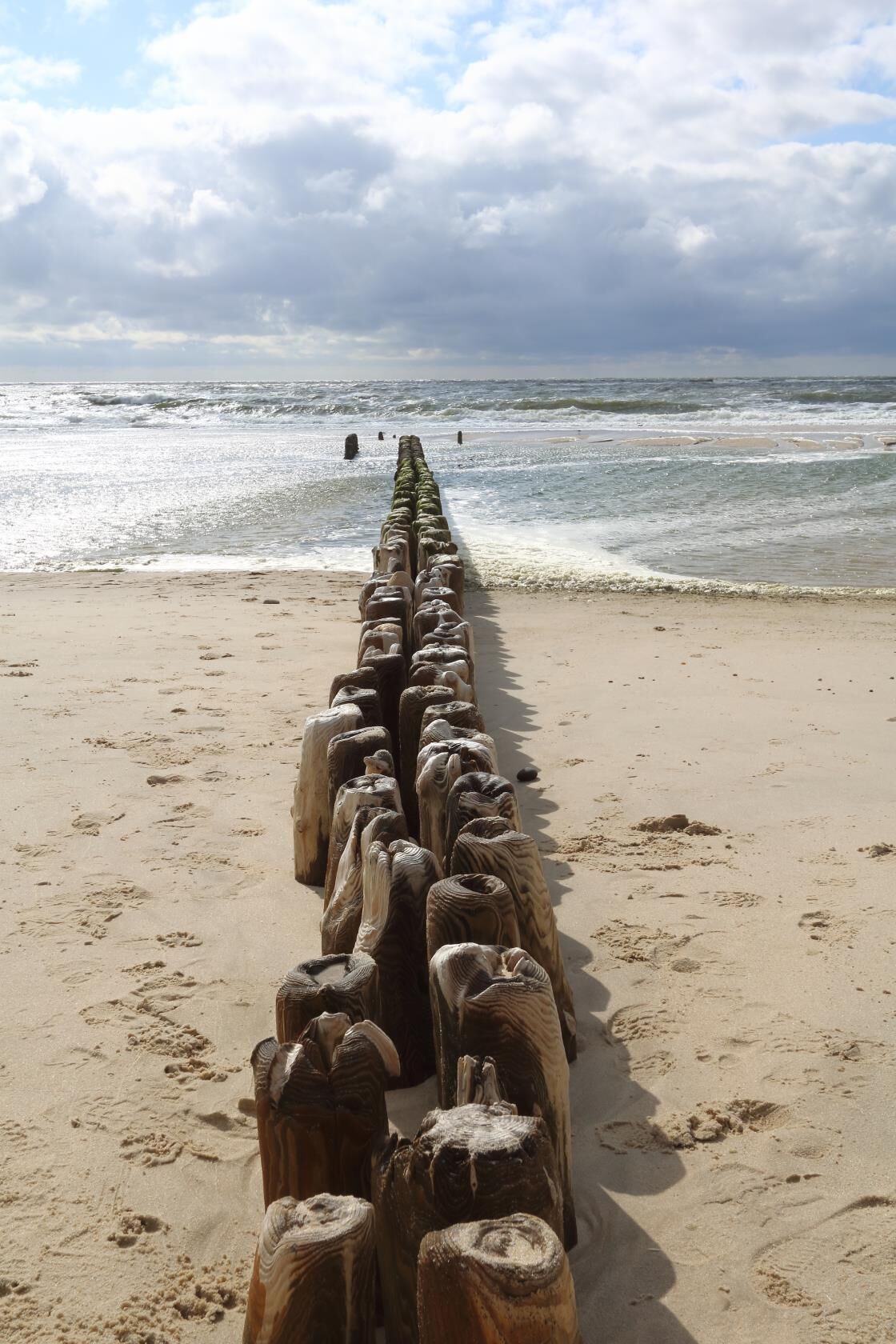 A wooden groyne on a sandy beach with the ocean in the background.