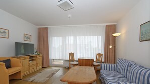 Una sala de estar con una mesa de madera, sofá, televisor y una ventana con cortinas.