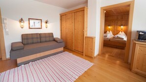 A room with a sofa, a wooden wardrobe, a bed, and a small table.