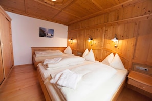 A wooden-paneled room with four beds, each with white linens and pillows, and wall-mounted light fixtures.