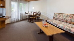 A cozy living room with a wooden ceiling, a sofa with floral upholstery, a dining table with chairs, and a television on a wooden stand. - Resort al Centro by Interhome (Breganzona)
