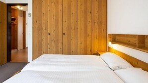 A bedroom with a wooden wardrobe, a bed with white bedding, and a nightstand with a lamp. - Resort al Centro by Interhome (Breganzona)