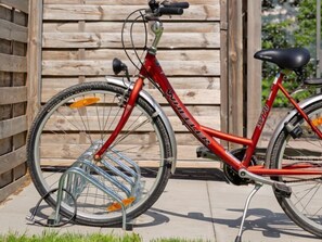 Un vélo rouge, doté d’un panier à l’avant et d’un porte-bagages à l’arrière, est garé contre une clôture en bois.