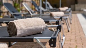 A row of sun loungers with towels placed on them, set on a paved area with a stone wall in the background. - Resort al Centro by Interhome (Breganzona)