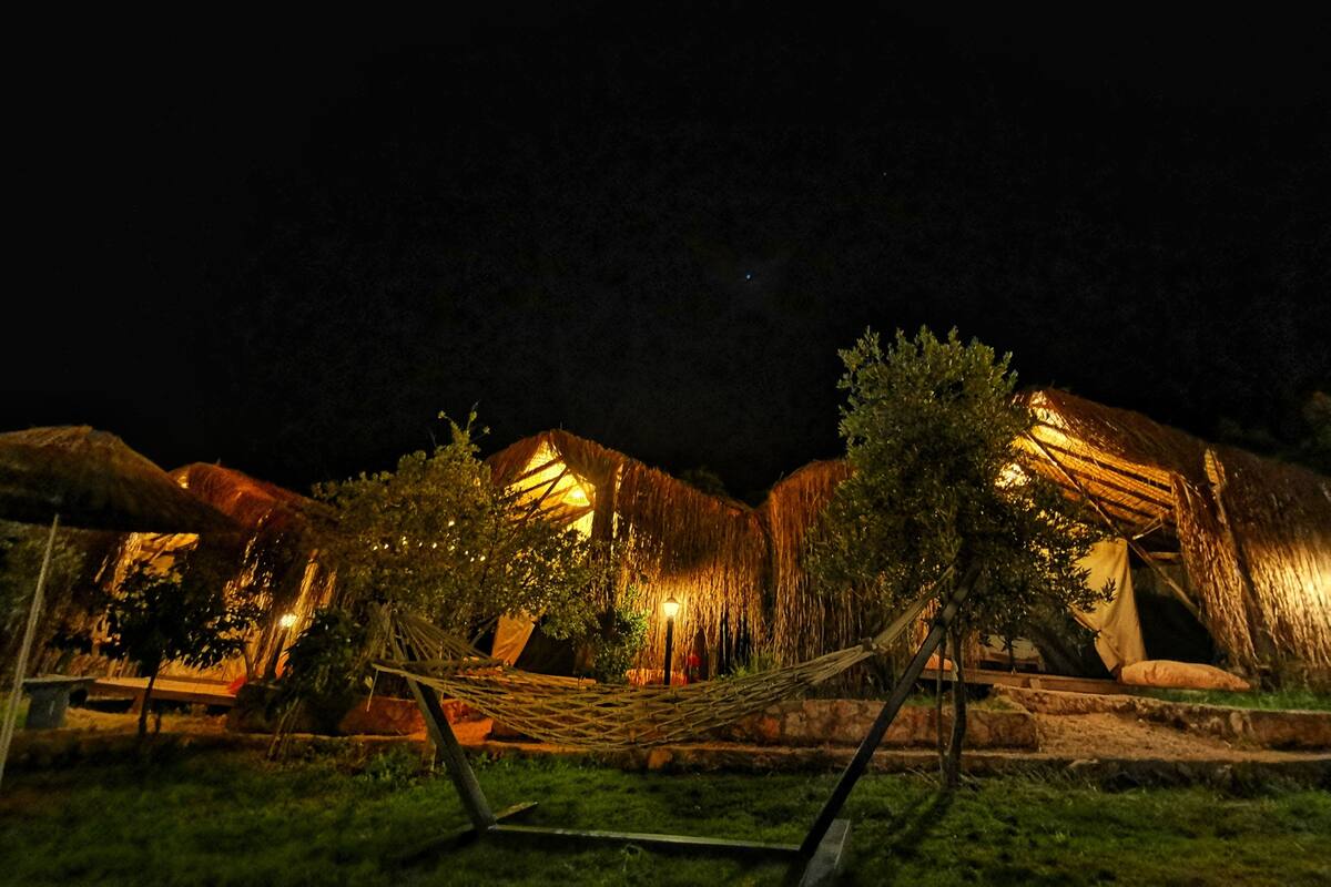 A series of thatched-roof buildings with warm lighting, a hammock, and a well-maintained lawn.