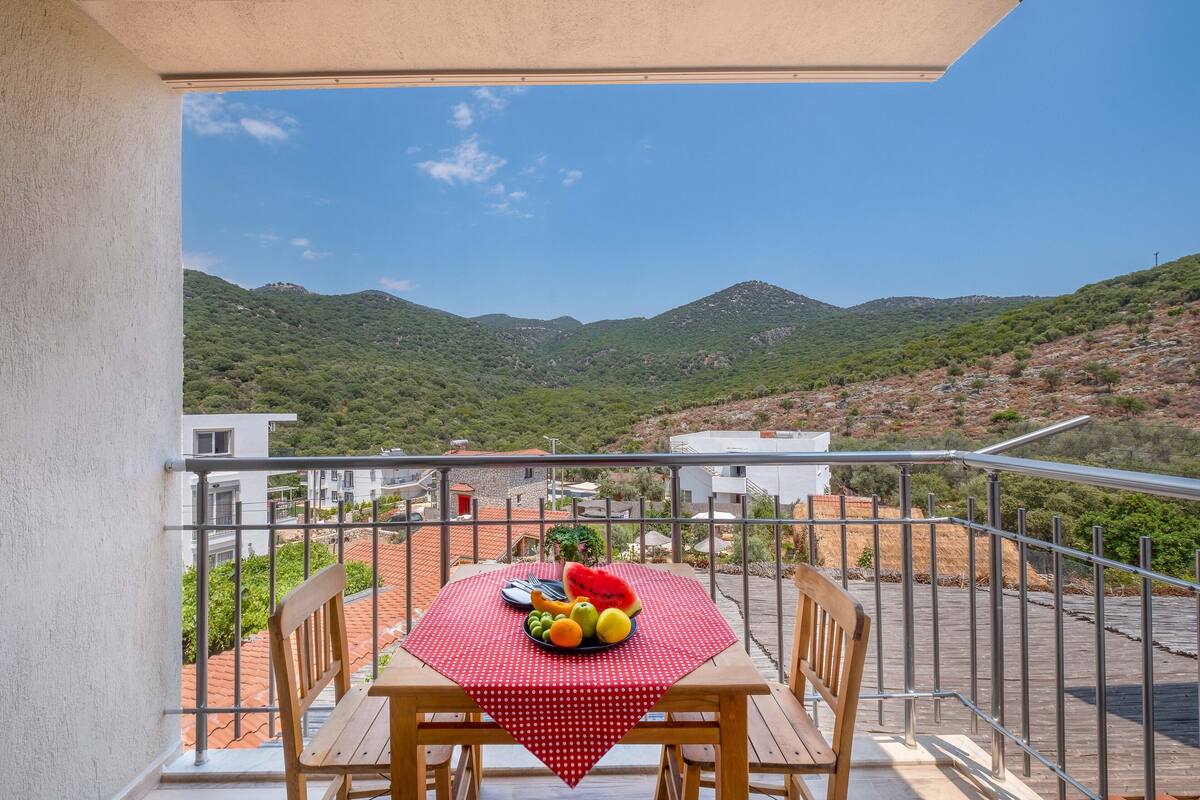 A balcony with a table set for a meal, overlooking a mountainous landscape.