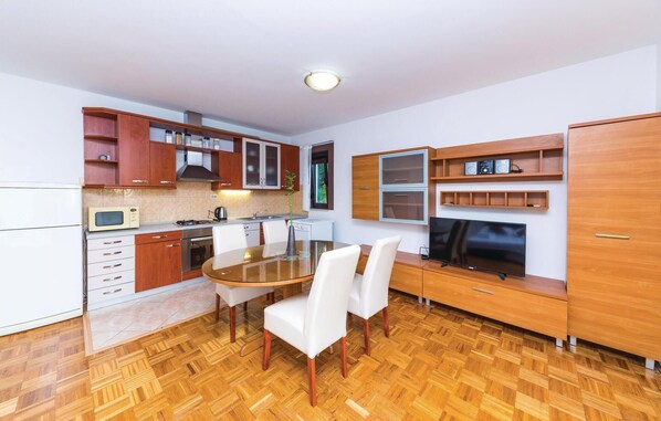 A compact kitchen with wooden cabinets, a microwave, a stove, and a dining area with a table and chairs. - 1 bedroom amazing apartment in Trogir (Trogir)