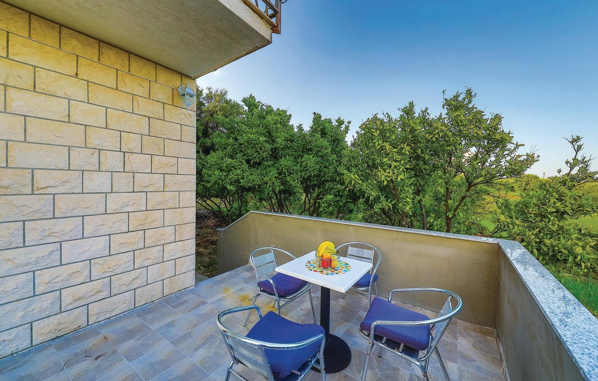 Une petite terrasse extérieure avec une table et quatre chaises, entourée d’un mur de briques et d’une végétation luxuriante.