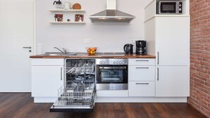 Ett modernt kök med vita skåp, en rostfri köksfläkt, en inbyggd ugn, en mikrovågsugn och en diskmaskin.