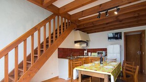 Eine Küche mit Holzbalken, einem Esstisch mit Stühlen, einem Kühlschrank und einer Mikrowelle.