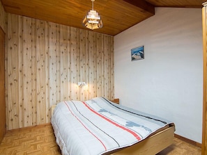 Un dormitorio con techo de madera, una cama con colcha a rayas, una lámpara fijada a la pared y un cuadro enmarcado.