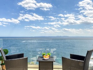 A balcony with wicker chairs and a table, overlooking a body of water and distant land under a partly cloudy sky. - Meda Chica by Interhome (Roses)