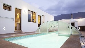 Ein modernes Gebäude mit einem von Glas umgebenen Schwimmbad, einer Treppe zu einer oberen Ebene und einem Berg im Hintergrund.