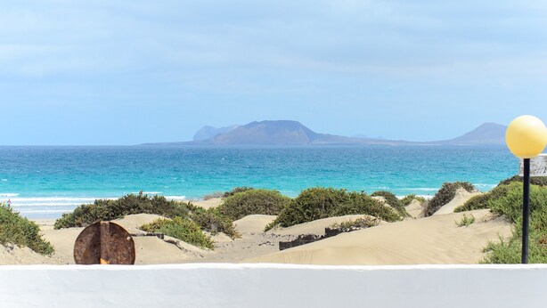 Eine Küstenlandschaft mit Sanddünen, blauem Meer und Bergen in der Ferne.