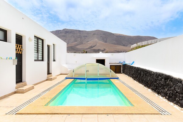 A swimming pool with a glass enclosure, white walls, and a view of a mountain.