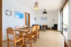 A dining area with a wooden table and chairs, a hanging light fixture, a television, and a view through a glass door.