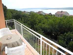 Enjoy the serene view of the water and forest from this balcony, featuring a table and two chairs.