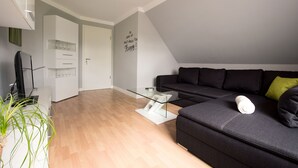 Een moderne woonkamer met een donkergrijze bank, een glazen salontafel en een witte kast.