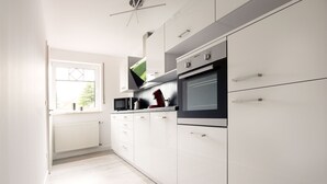 Een moderne keuken met witte kasten, een inbouwoven en een raam met uitzicht op bomen.