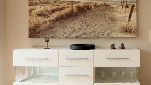Een modern, wit kastje met een glazen vitrine en een strandafbeelding erboven.