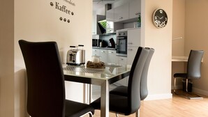 Een moderne eetruimte met een glazen tafel, zwarte stoelen en een keuken in de achtergrond.