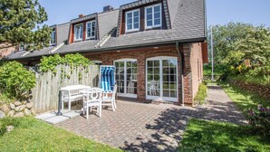 A two-story house with a brick exterior, large windows, and a patio area with outdoor furniture.