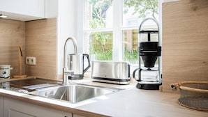 A modern kitchen with stainless steel appliances, a coffee maker, and a window with a view of greenery.
