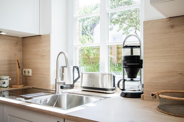 Une cuisine moderne équipée d’appareils électroménagers en acier inoxydable, d’une machine à café et d’une fenêtre donnant sur un espace verdoyant.
